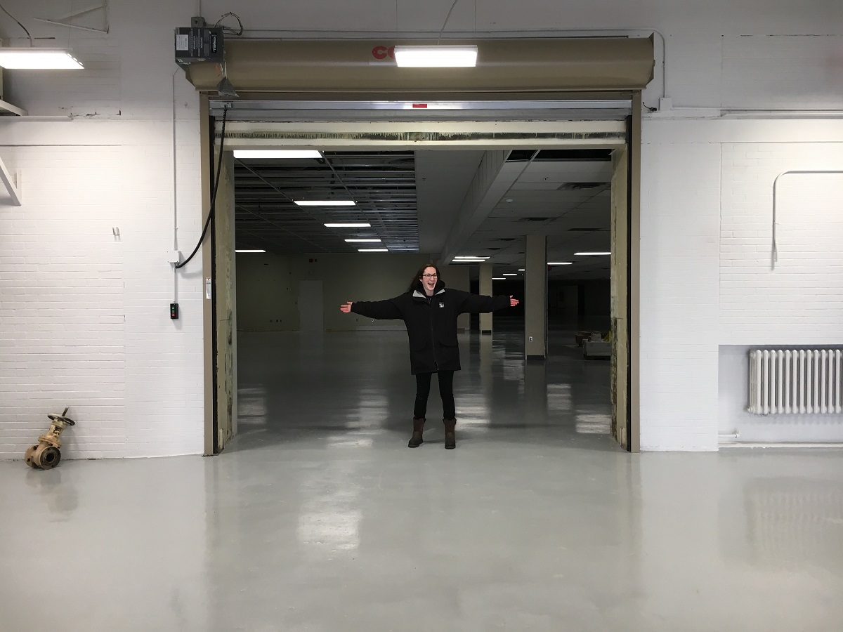 A person stands with arms outstretched in a large doorway connecting one large, empty room to another