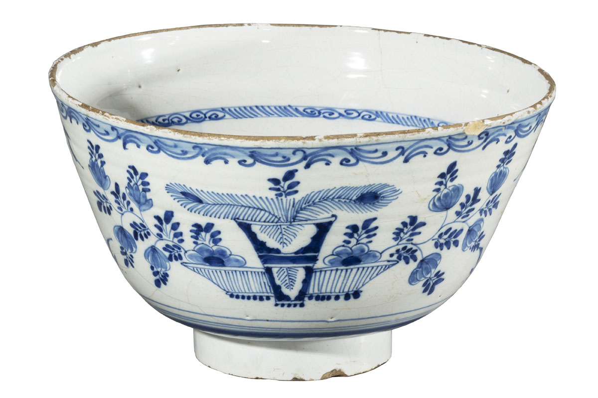 White bowl with narrow base and body sloping outward to a wide mouth, with blue decorations of flowers, plants, and bowls of fruit