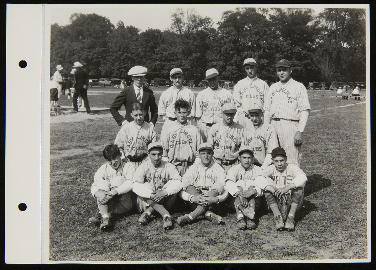 A group of boys and men in baseball uniforms pose for a photo in front of a baseball diamond