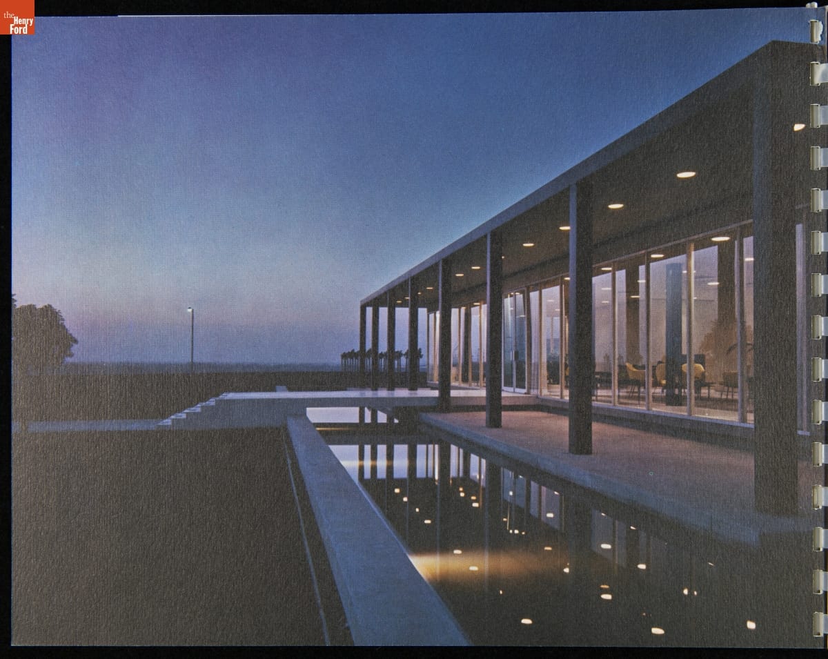 Low, modern glass and concrete building with patio, columns, and pool outside, pictured at dusk