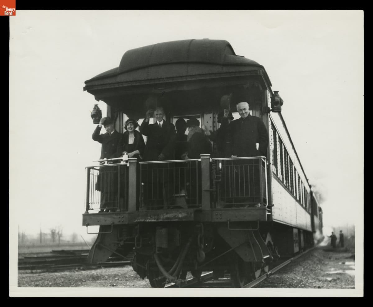 Edsel and Eleanor Ford, Henry and Clara Ford, and Mina and Thomas Edison on the Private Railroad Car "Fair Lane," circa 1923 Several people stand on the back platform of a railcar, some waving