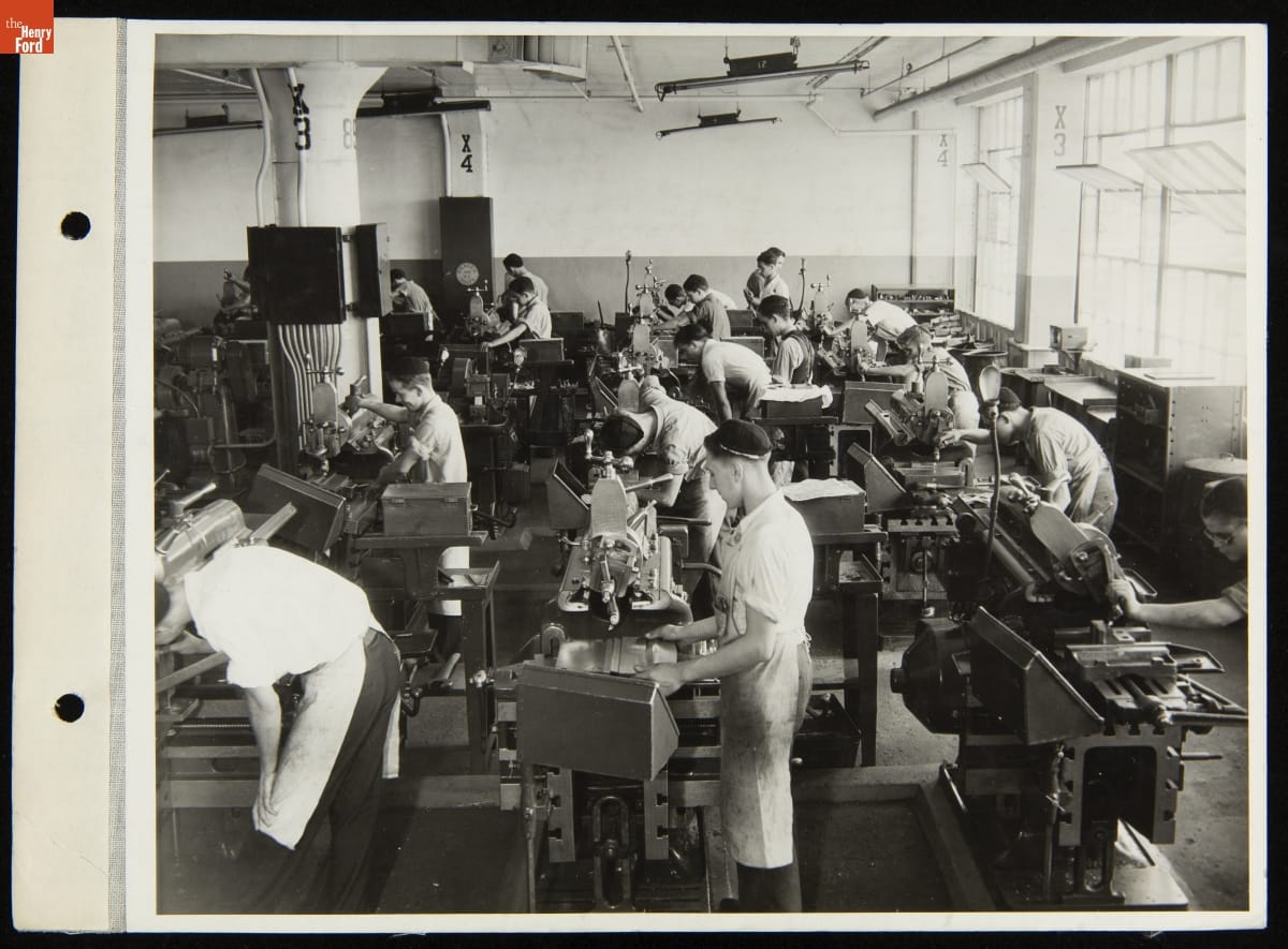 Group of boys and young men work at machines in crowded room