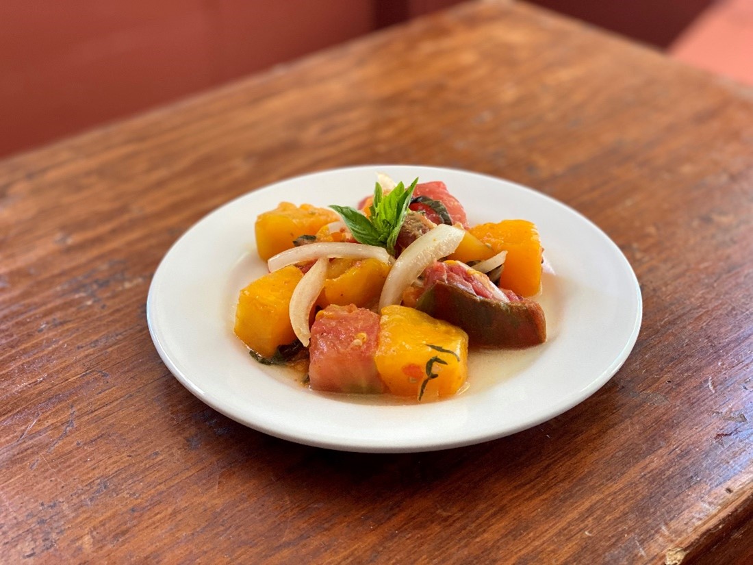 A plate holds a salad of large chunks of multicolored tomatoes in dressing, with a sprig of basil in the middle