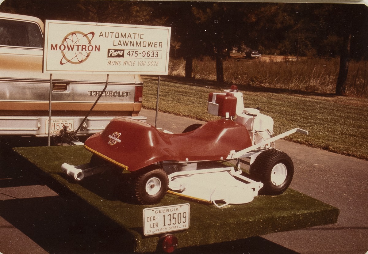 Lawmower on trailer behind truck, with sign containing text
