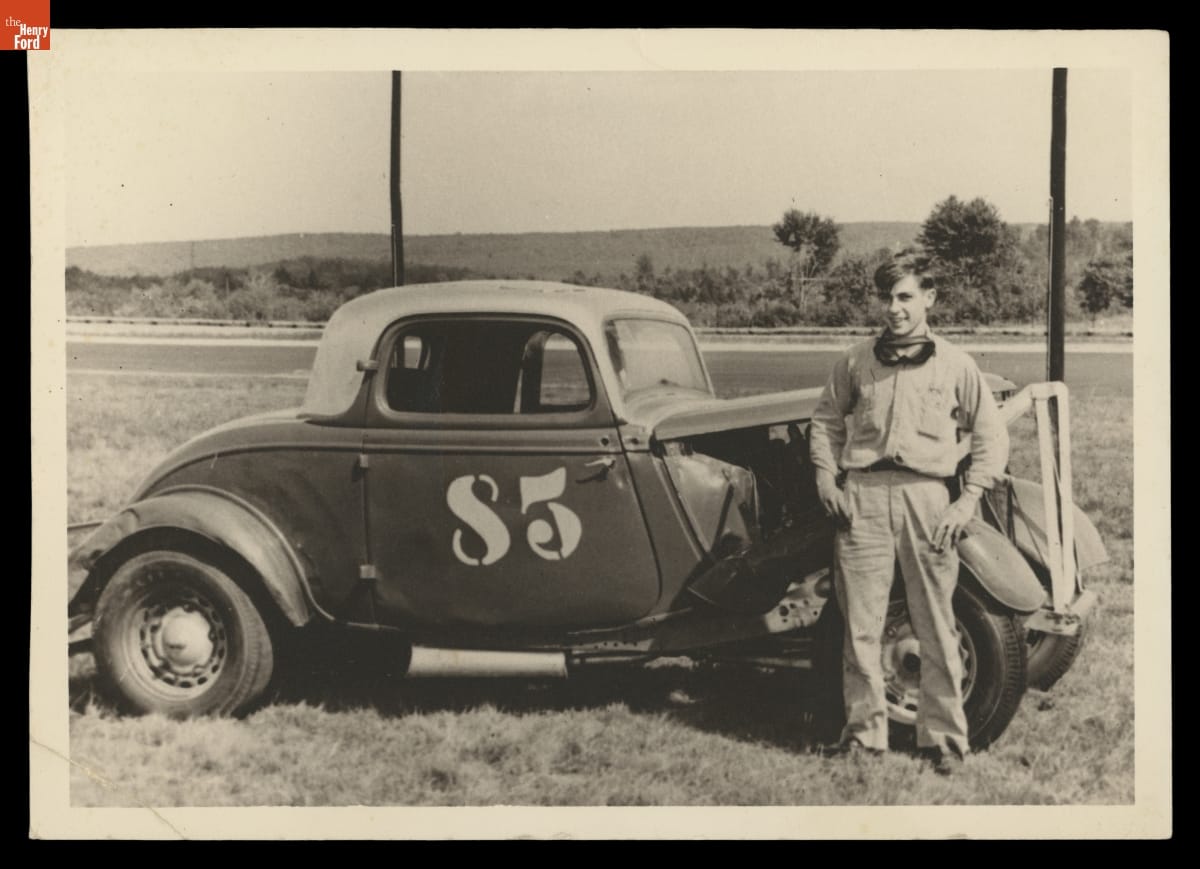 Boy stands next to car in field