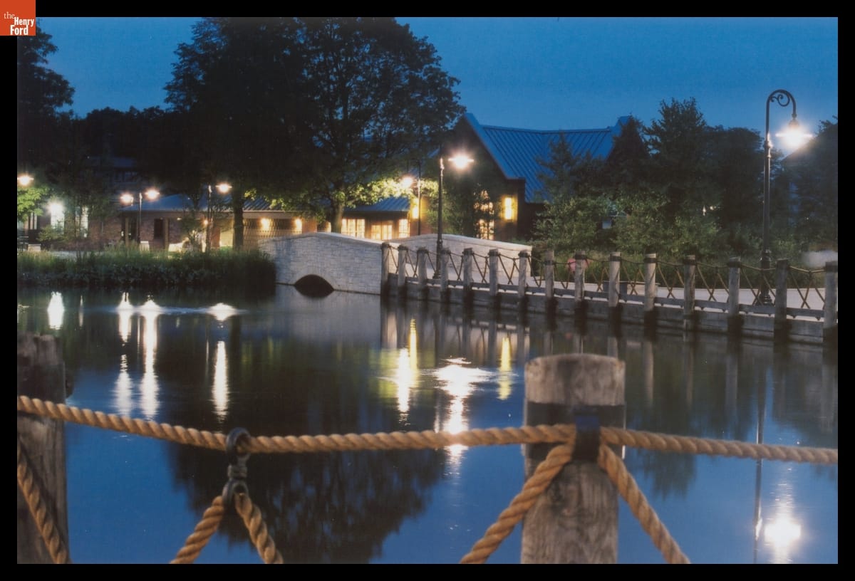 Pond at dusk, surrounded by wood and rope rails, with building(s) in the background