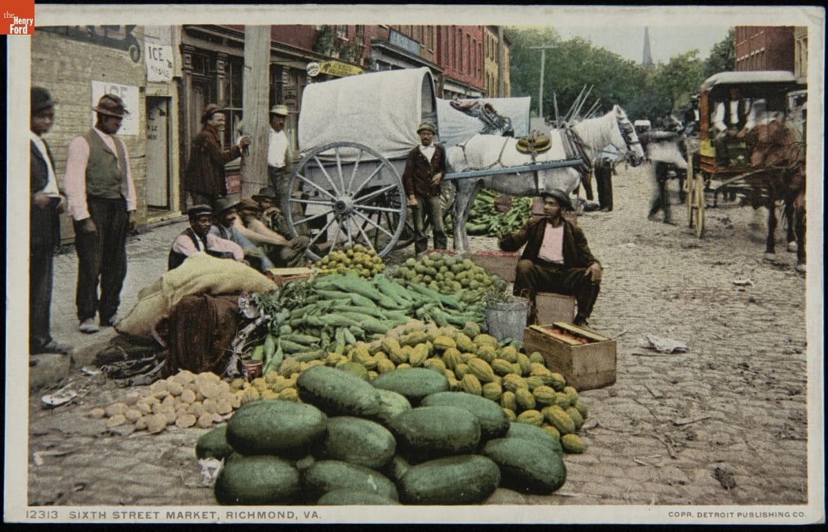 Sixth Street Market, Richmond, Va., 1908-1909 Men of color sit and stand around a piles of different vegetables at one side of a cobblestone street with buildings and horses and carriages behind them