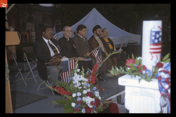 GIF cycling through images of large crowd of people, many with American flags or candles, and speakers on a stage