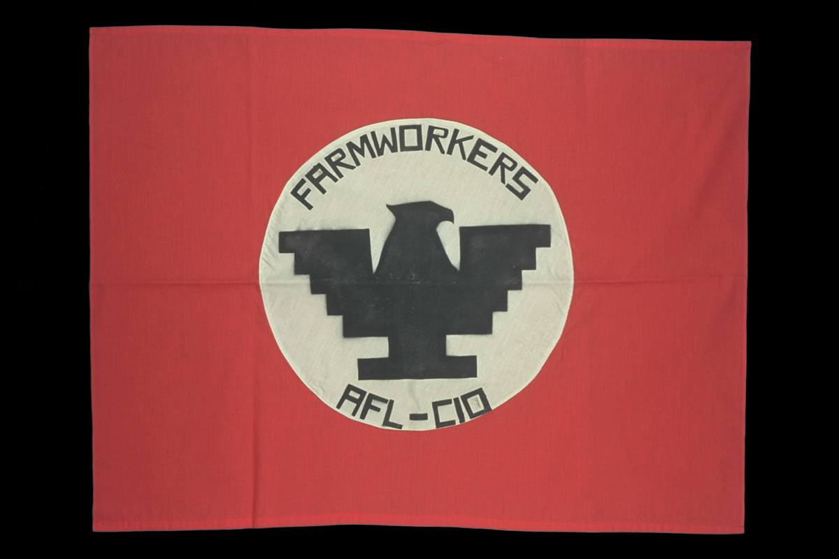 United Farm Workers Flag, circa 1970 Red flag with white circle in middle containing stylized black eagle and text "FARMWORKERS AFL-CIO"