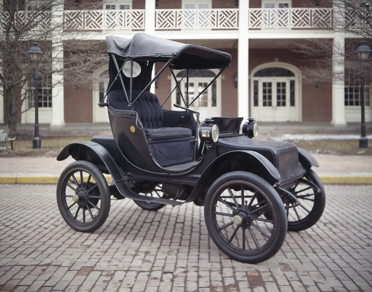 1912 Baker Electric Victoria, Used by Five First Ladies of the United States Small, largely open two-seater early automobile parked in front of a red brick building with white columns