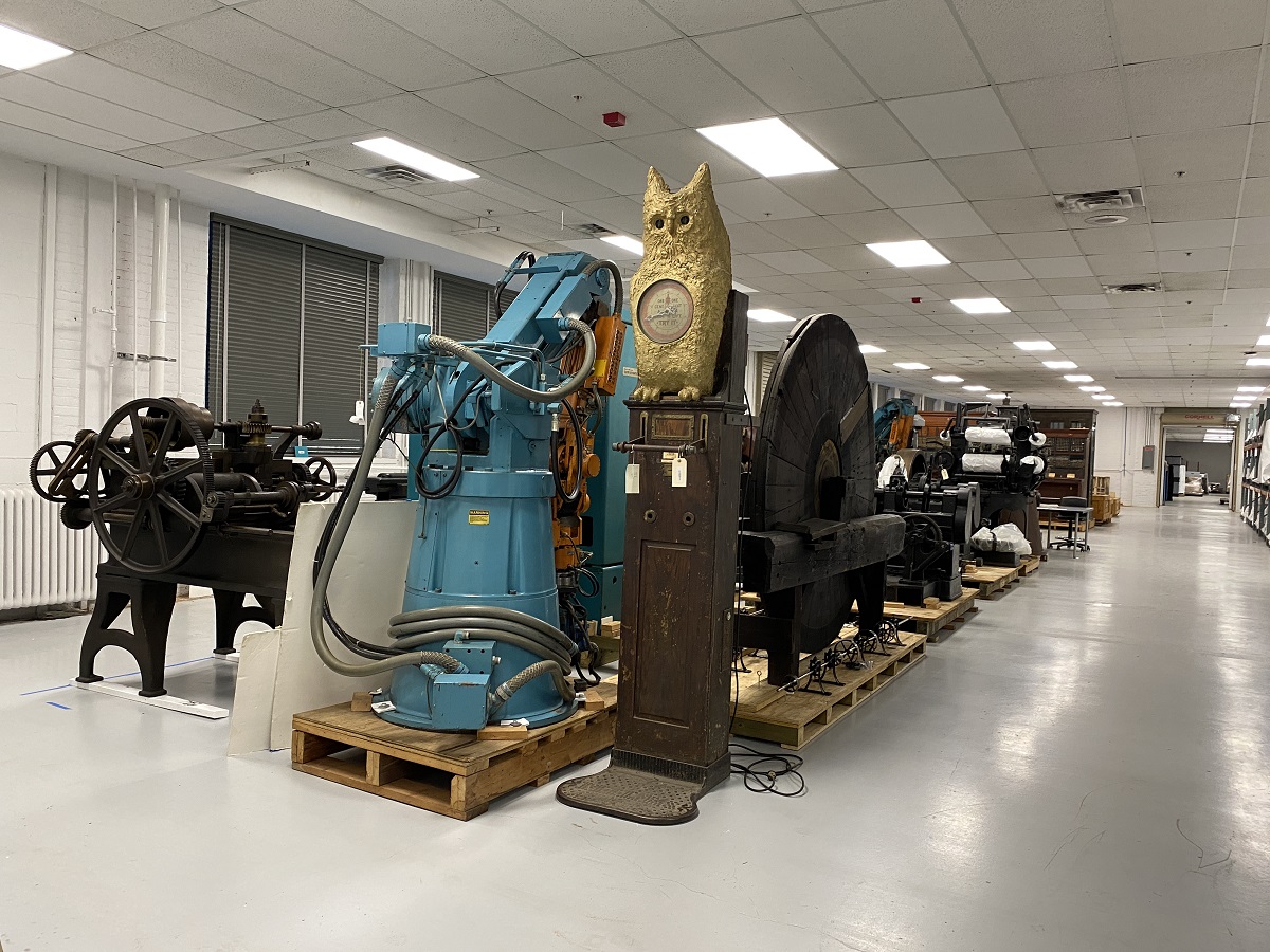 A variety of large objects sit on the floor or on pallets in a row in a large room