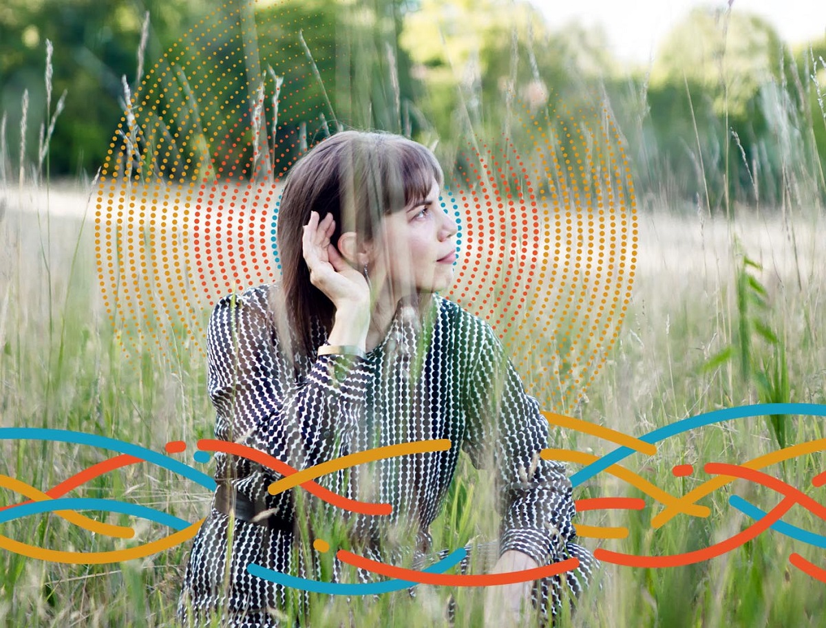 Woman in black-and-white printed outfit sits in field with hand to her ear