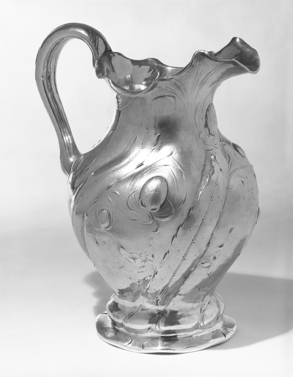 Silver pitcher with swirling decorative images, including octopus