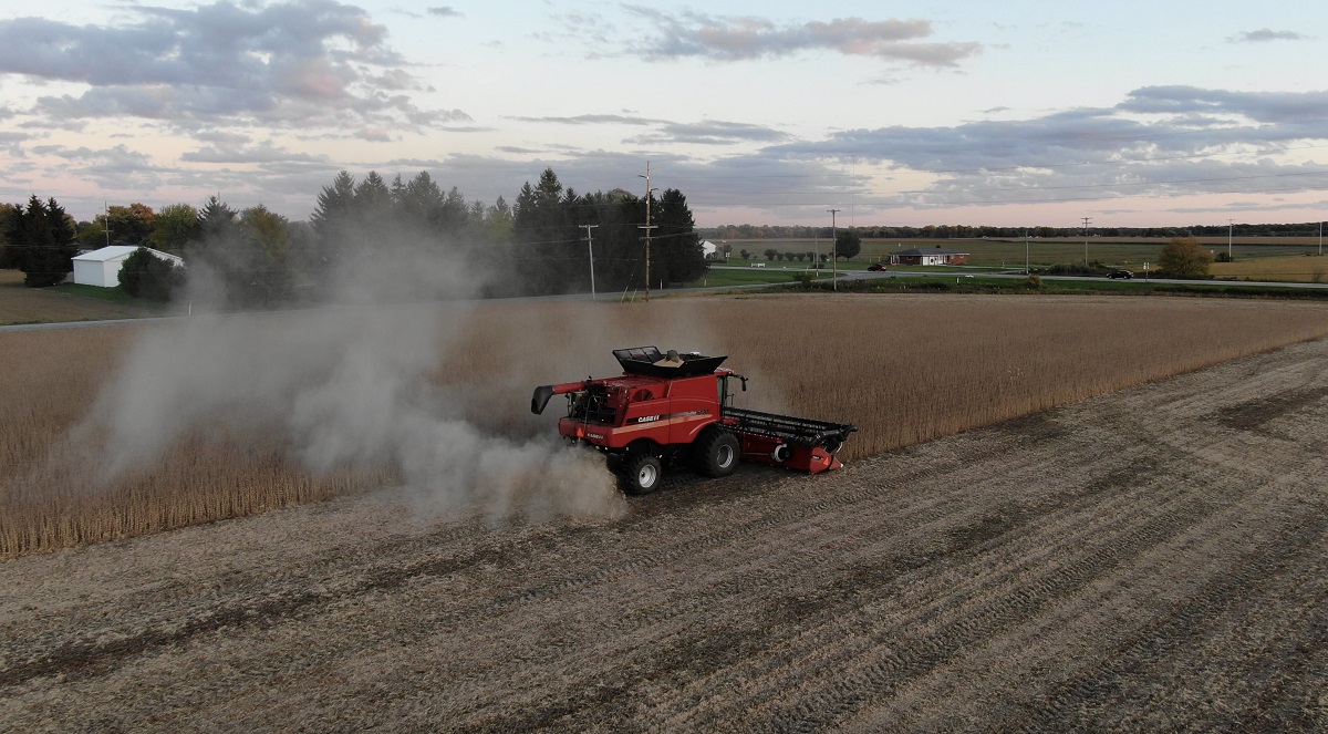 Wheeled red machine trailing dust cloud in a half-harvested field