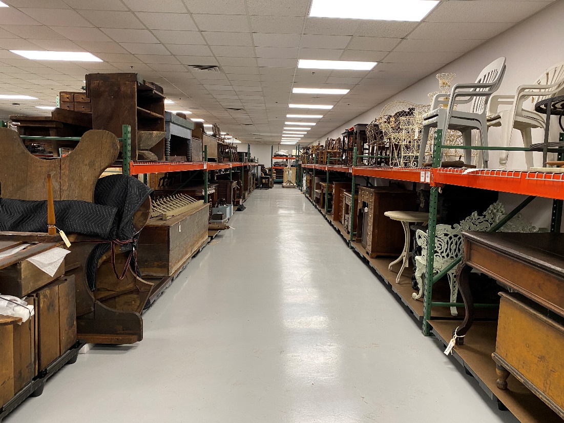 View down aisle with pallet racking on either side filled with chairs, desks, shelves, and other furniture
