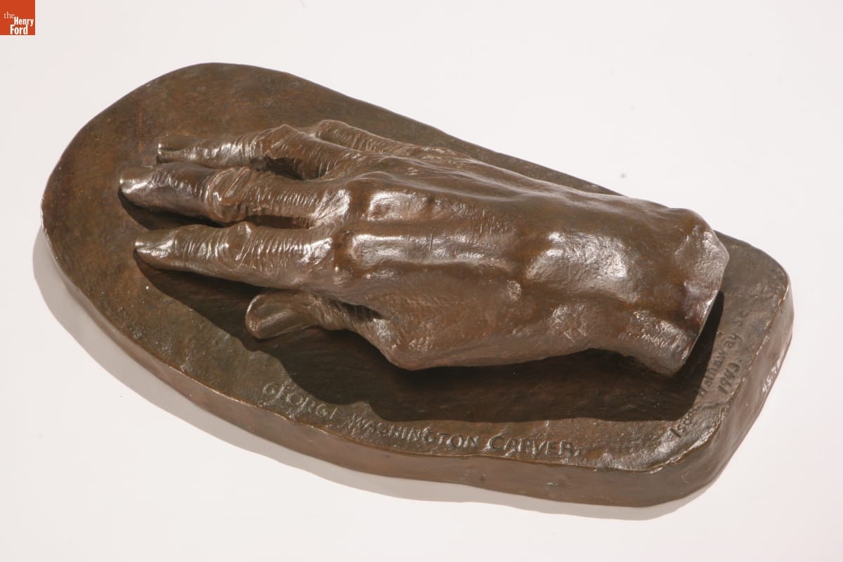 Brown sculpture of hand on flat surface; also contains text