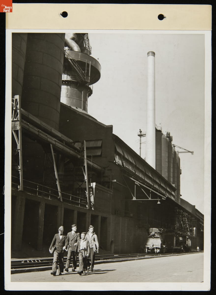 Four boys  and young men walk alongside a large factory building