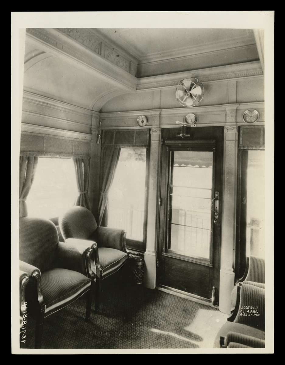 Black-and-white photo of room showing two chairs, windows, and glass door