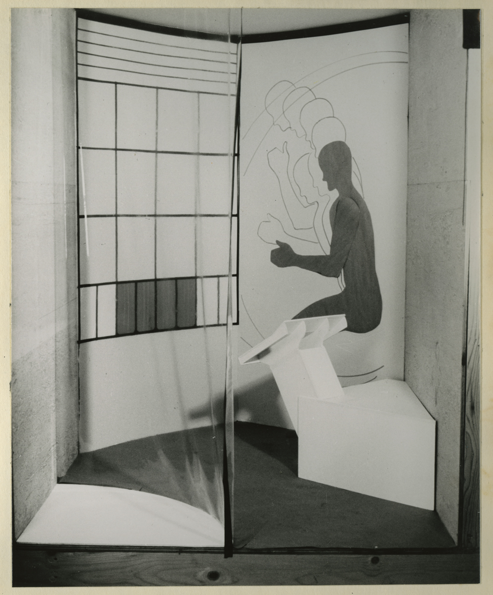 Space with arc-shaped plastic enclosure, geometric pattern on walls, and silhouette on wall of figure squatting piece of equipment or furniture