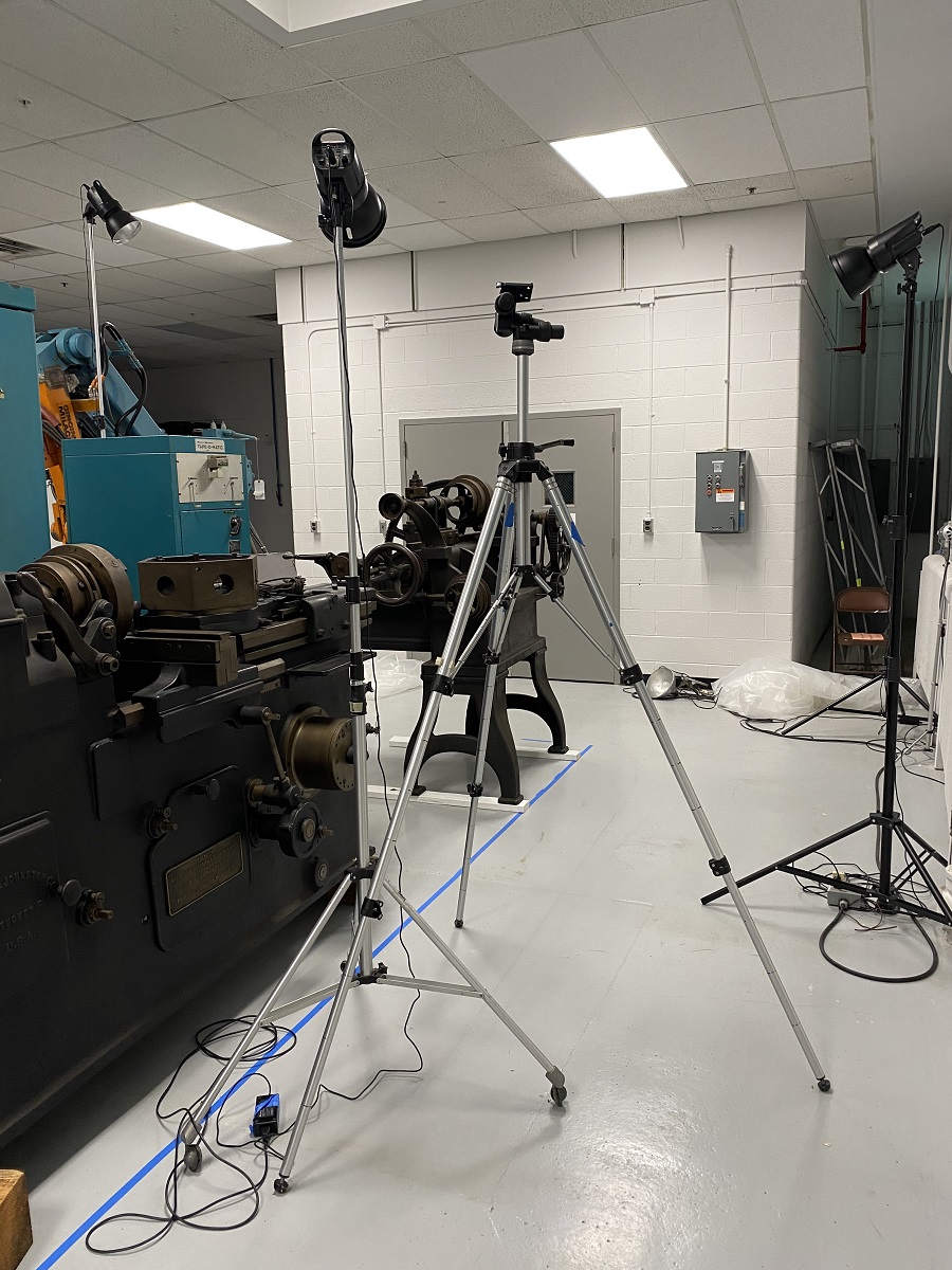 Tripods with lights pointed at machinery, with more machinery at side