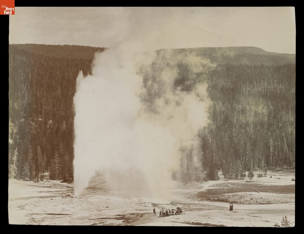 Old Faithful Geyser, Upper Geyser Basin, Yellowstone National Park, 1905 Black-and-white photo of geyser spewing water and steam into the air as people look on; vast pine forest in the background