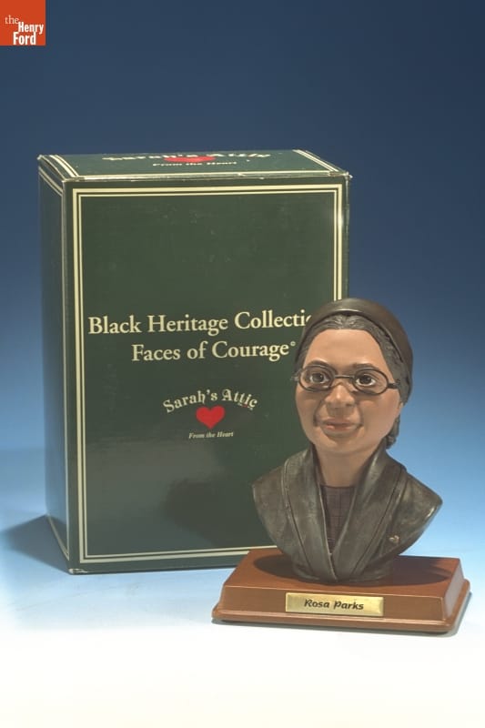 Small statue of woman's face and partial torso on base with text; sitting next to green box with text