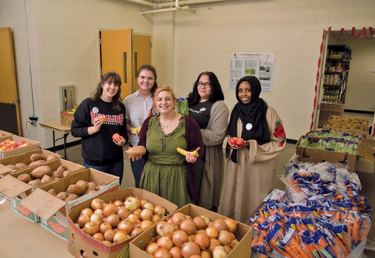 Five women hold produce behind tables covered in boxes full of vegetables