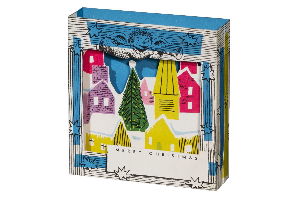 Three-dimensional paper card with a frame and angel surrounding a scene of houses and a Christmas tree in snow