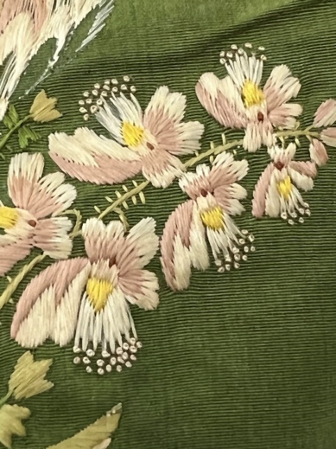 Close-up of embroidery Moss-green fabric with floral embroidery in pinks and yellow