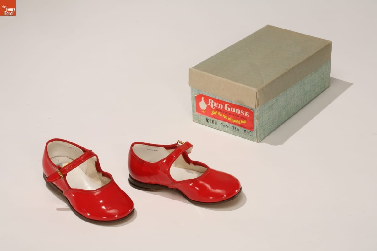 Red Mary Janes, 1960-1970 Shiny red shoes with a strap that would fall just in front of the ankle; blue shoebox next to them