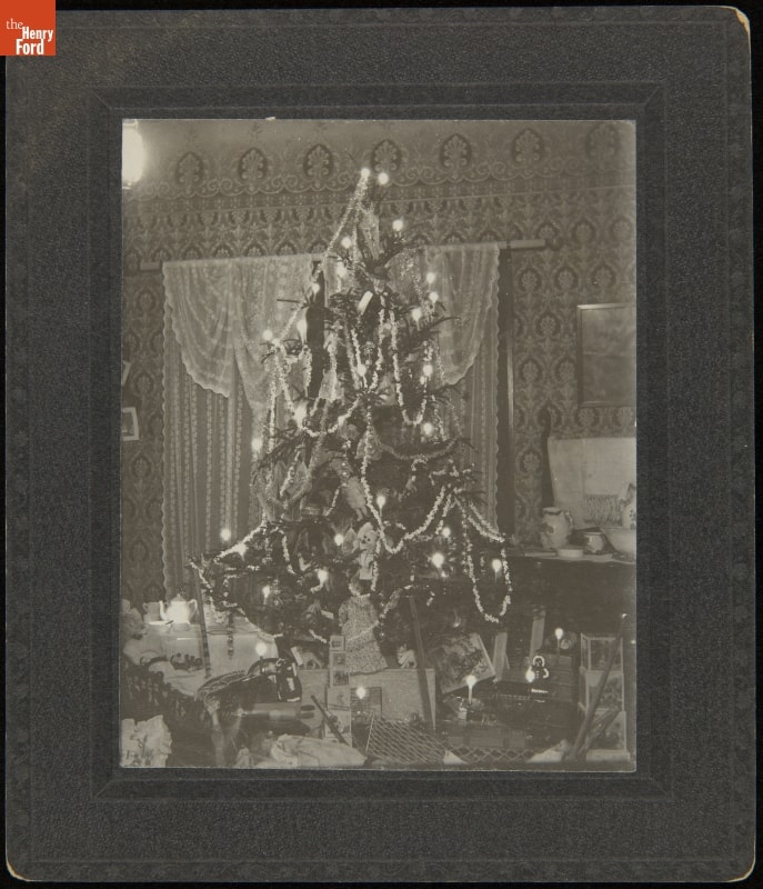 Christmas Tree Decorated with Candles, Popcorn Strings and Toys, circa 1900 Matted black-and-white photo of a Christmas tree covered in decorations and surrounded by packages
