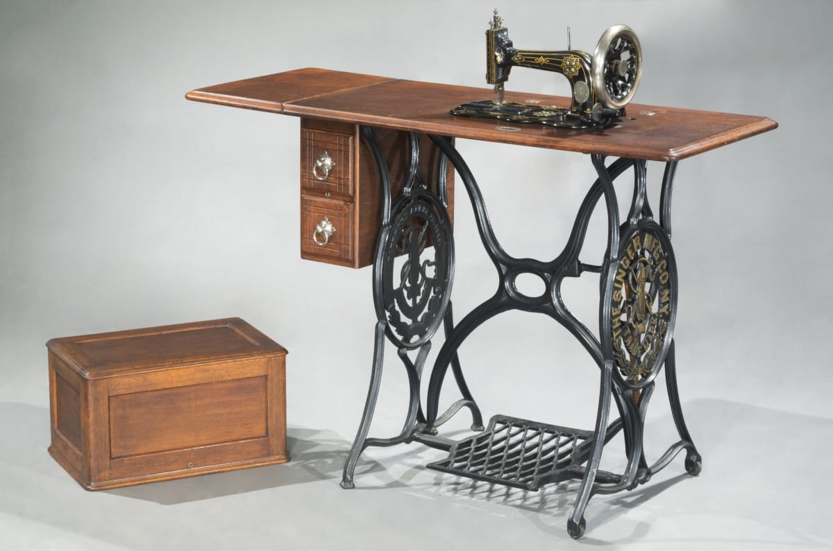 Sewing machine built into wooden table with intricate, decorative metal base