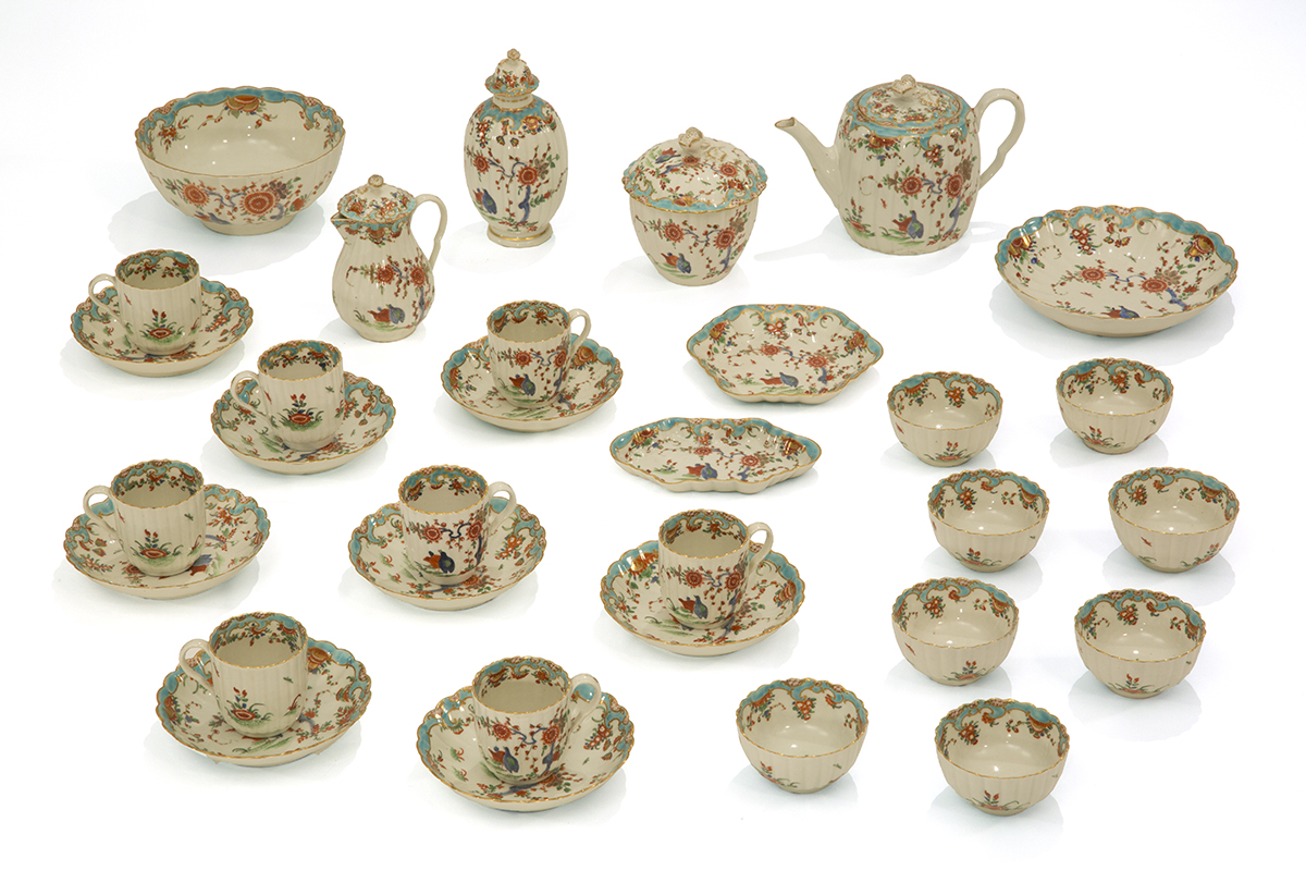 Photo of extensive cream colored tea service with intricate multicolored flowers and birds; set contains cups and saucers, small bowls, teapot, and several other miscellaneous dishes