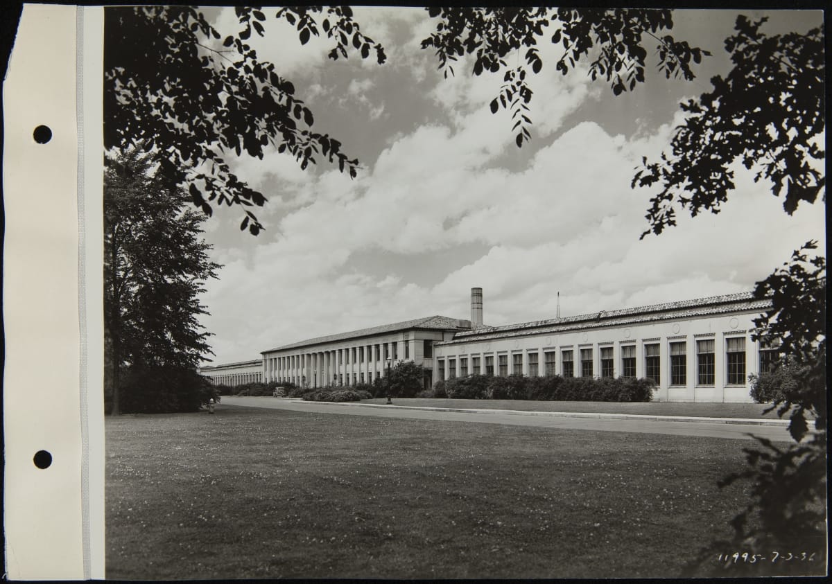Black-and-white photo of long, low building across a grassy lawn