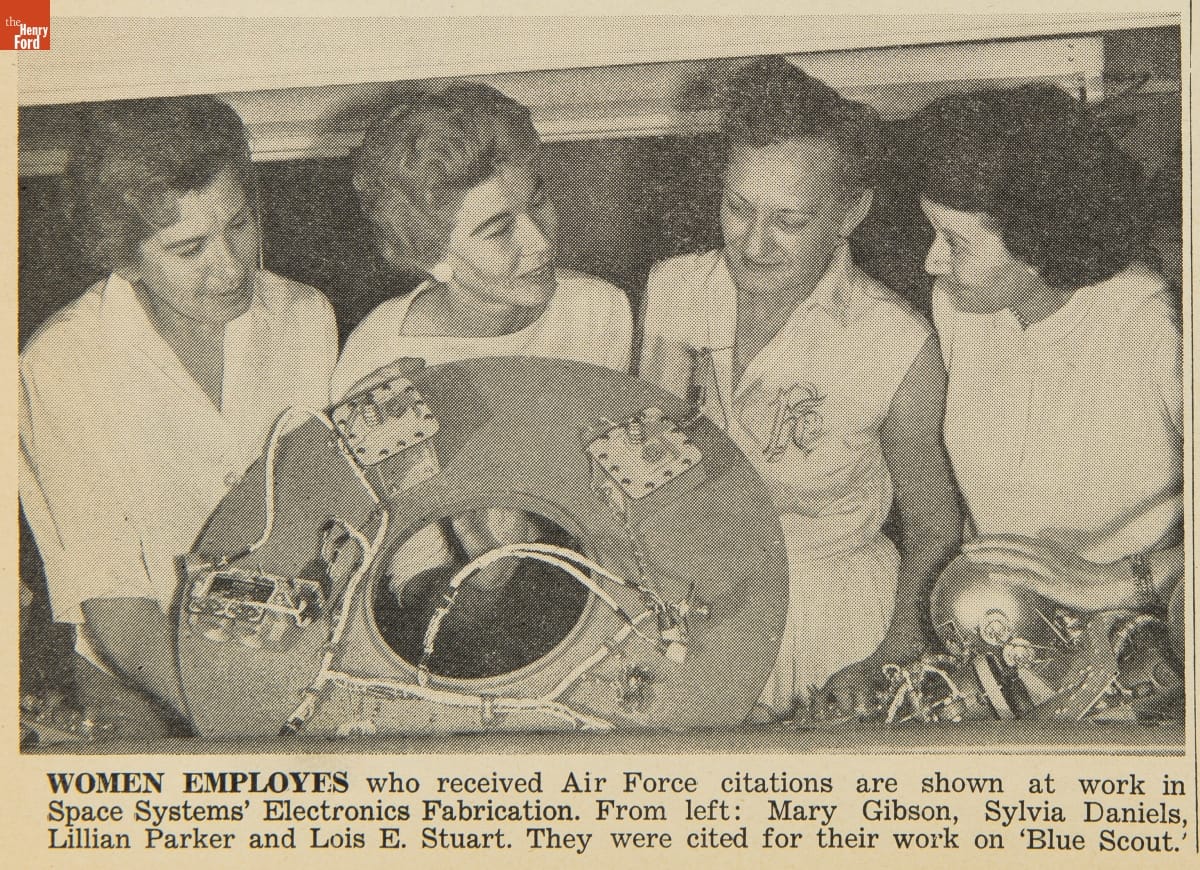 Black-and-white photo of four women with large, round component with wiring; also contains text