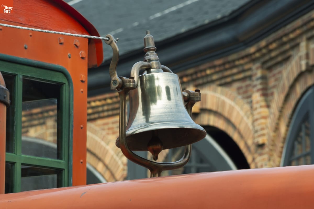 Silver bell apparently mounted on top of orange locomotive (barely visible in picture) in front of a brick building