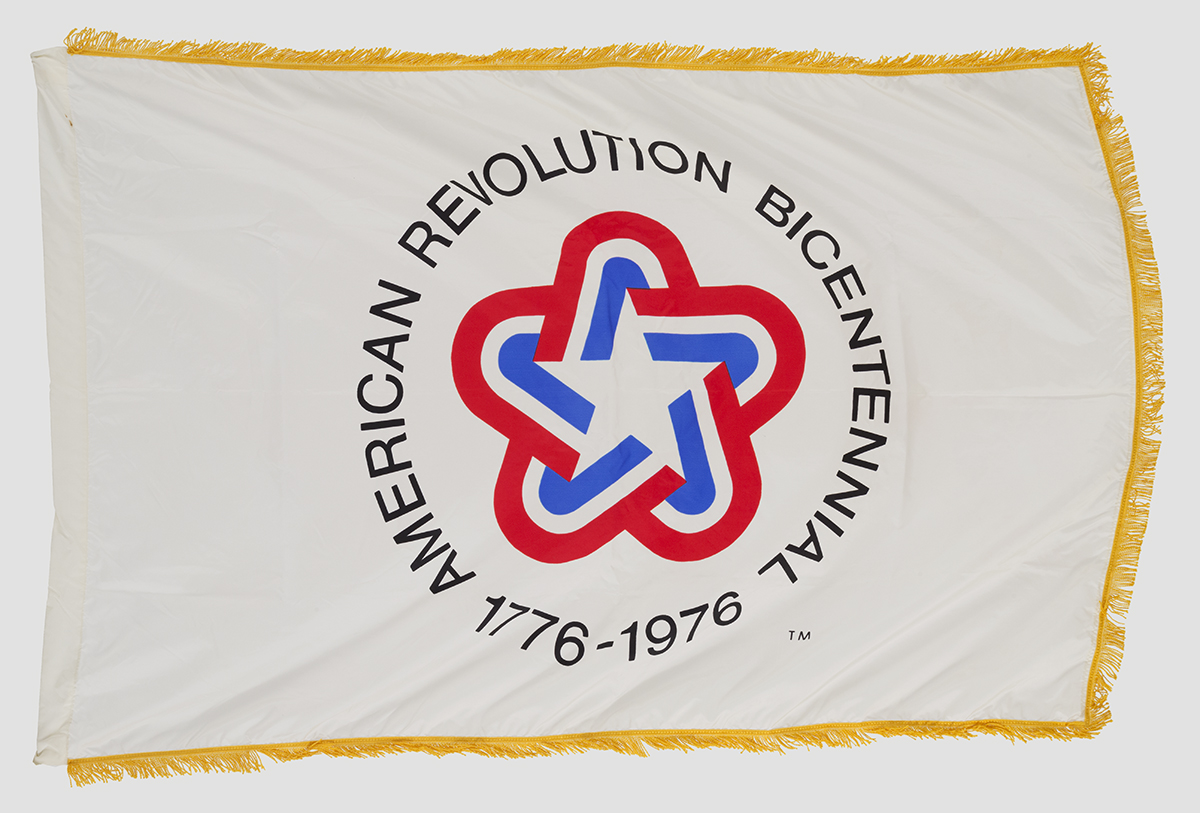 Gold-fringed white flag with rounded star in red, white, and blue and text "American Revolution Bicentennial 1776-1976"