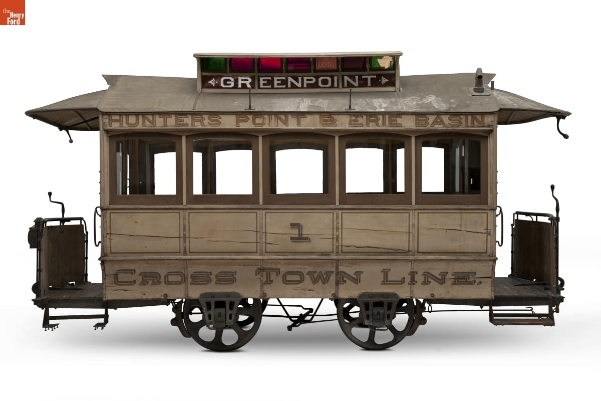 Wooden streetcar on metal wheels, with colored glass in top turret and text on side