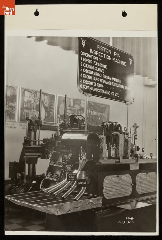 Machine on display under a sign with text, with images along wall behind