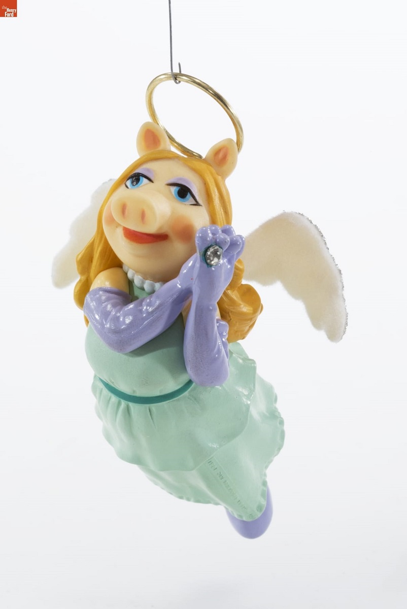 Christmas ornament of pig in blue gown with purple shoulder-length gloves, blonde hair, and pink angel wings