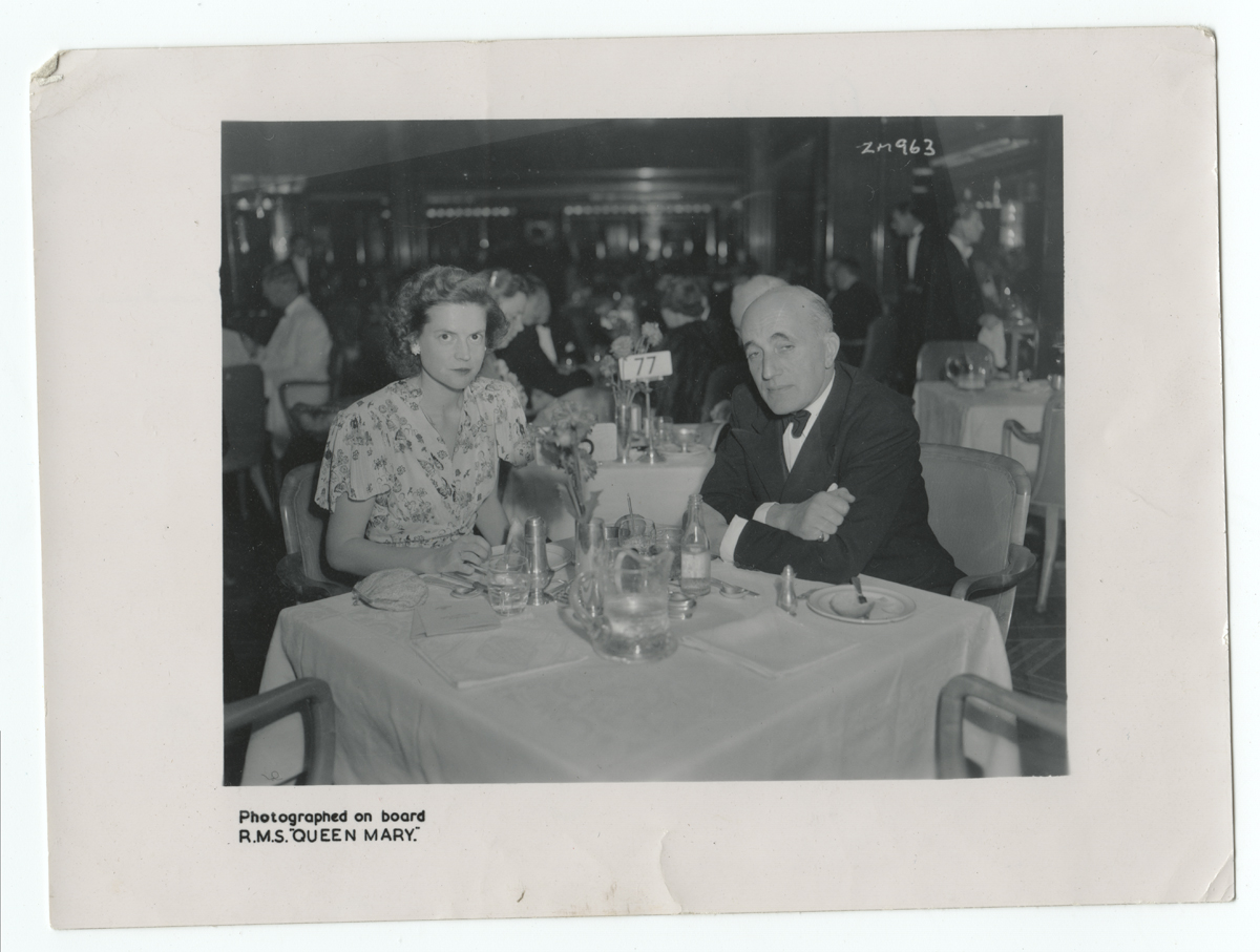 Black-and-white photo of a woman and man seated at a tablecloth-covered table among other diners
