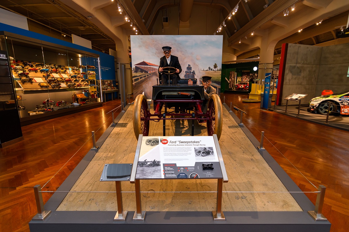 Museum display with open car with mannequin behind wheel; other displays visible nearby