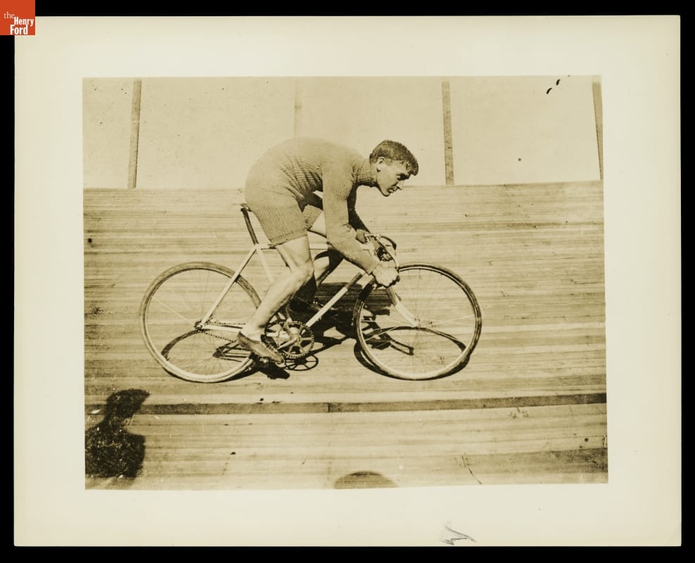 Man hunched over riding a bicycle on a steeply-tilted wooden track