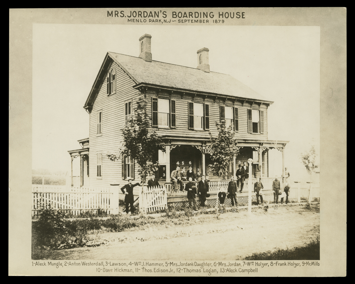 Mrs. Jordan's Boarding House, Menlo Park, N.J.--September 1879 Black-and-white photo of two-story wooden house with people on porch and standing by and in front; also contains text