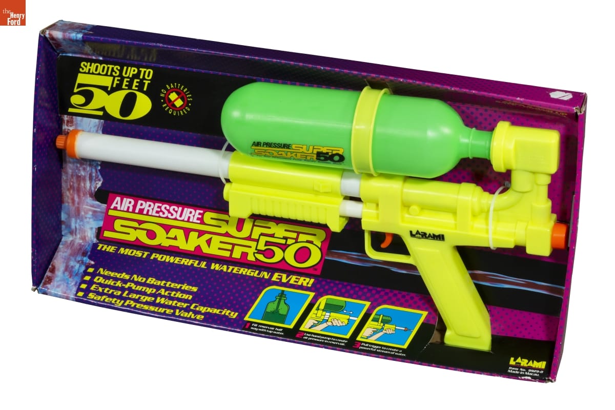 Large yellow and green water gun in black and purple cardboard packaging; also contains text