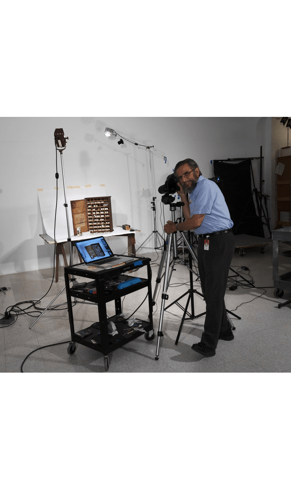 GIF cycling through a number of images of person with camera set up photographing a cabinet full of small packages