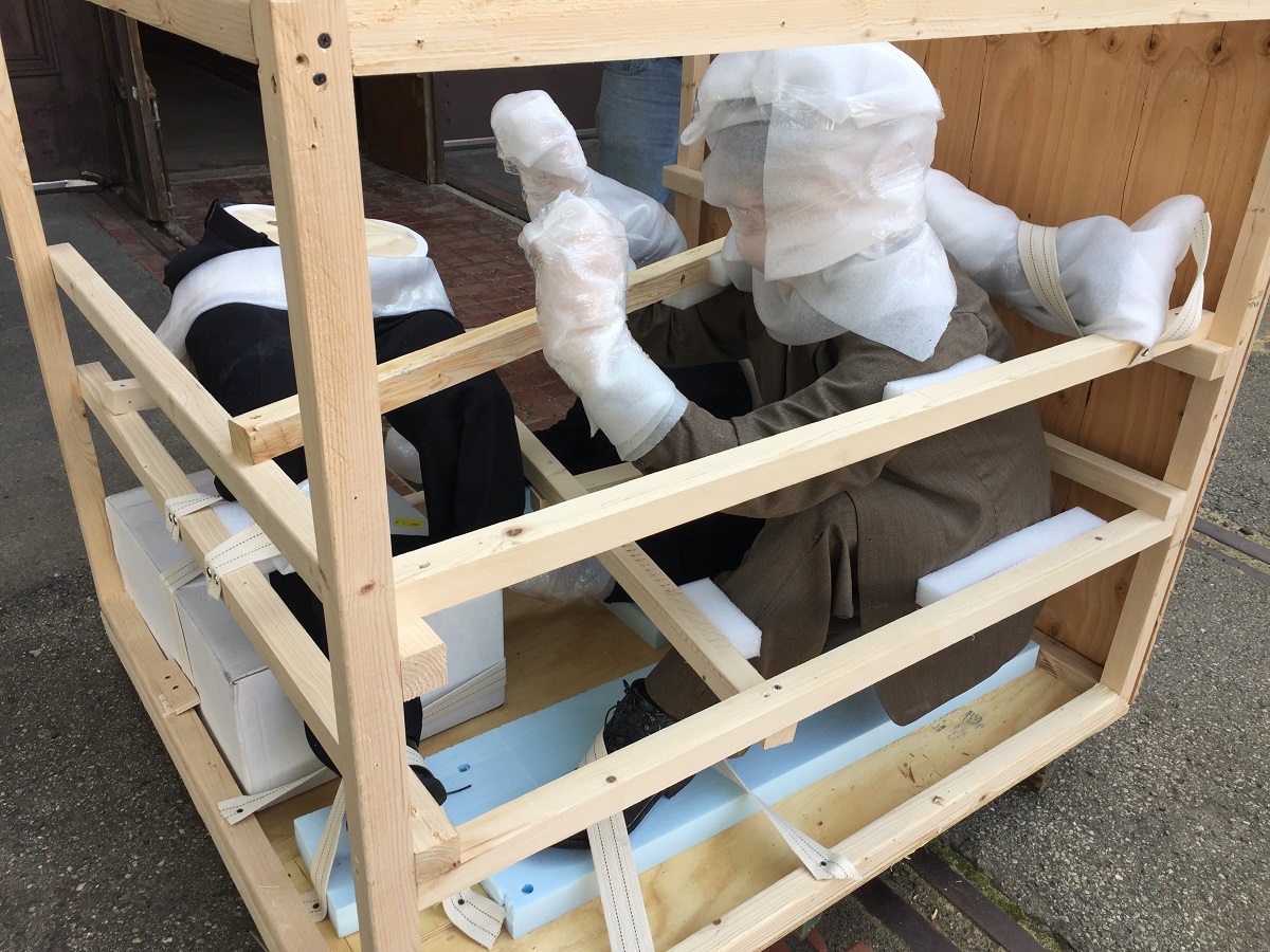 Open crate with two human-like figures swaddled in packing material