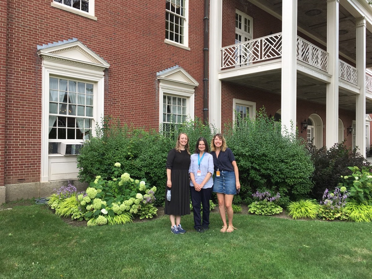 Jennifer Junkermeier-Khan, Debra Reid, and Ayana Curran-Howes Three women pose in front of flowerbeds and a red brick building with white-pillared porch and balcony