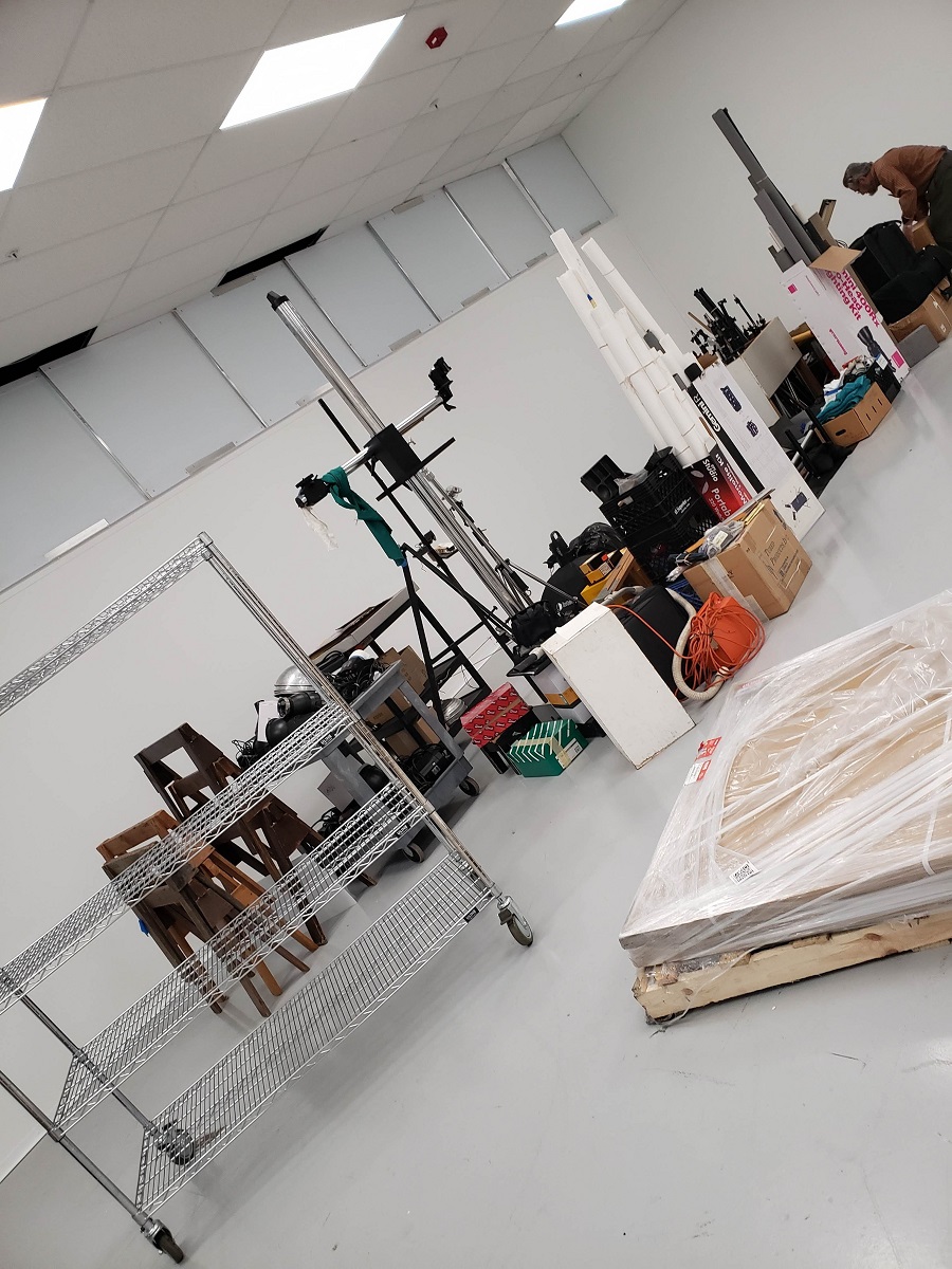 Unloading and organizing our equipment in the new studio Angled photo of furnishings and equipment lined up in a clump in the middle of a white room