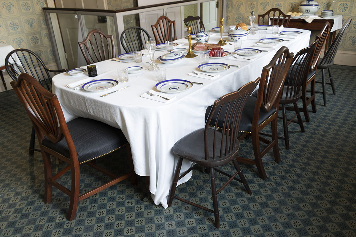 Long set table with mismatched chairs in room with patterned carpet and wallpaper